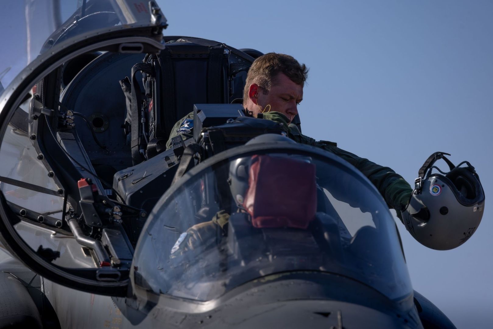 Pilot seated in a jet cockpit holding a flight helmet