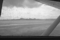Rain-speckled aircraft window overlooking cloudy water and distant hills
